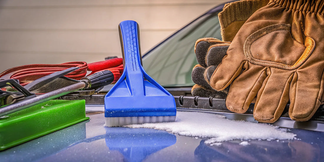 Winter car accessories including ice scraper, snow brush, and emergency gear arranged on a flat surface