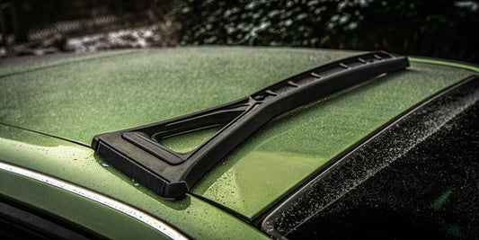 An unbreakable car scraper clearing thick frost from the roof of a green car.
