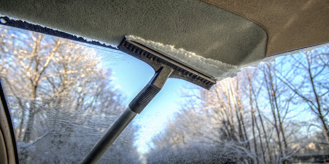 An oversized snow and ice scraper clearing a car windshield covered in heavy snow.