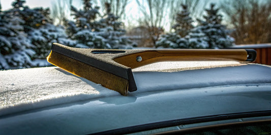 A heavy-duty car snow scraper clearing thick ice and snow from a car windshield.