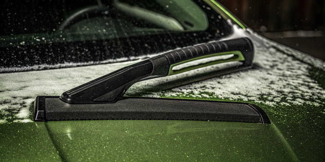 A custom snow and ice scraper with a brand logo clearing a snowy car windshield.
