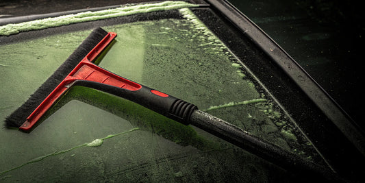 Close up of an oversized ergonomic red and black ice scraper on a frosty car windshield on a winter morning