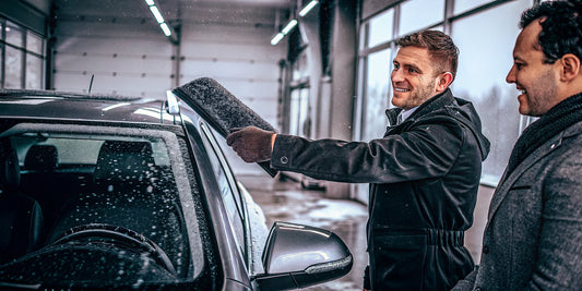 Car dealership salesperson handing a custom-branded premium ice scraper to a customer in a showroom during winter