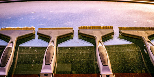Four ergonomic ice scrapers being reviewed and tested on a frosty car windshield.