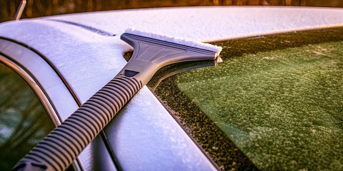 A hand in a glove ice scraper clearing light frost from a car windshield.