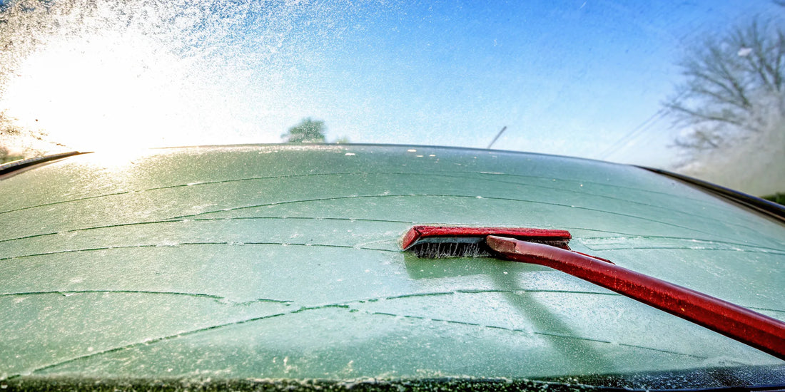 Frost-covered car windshield with one side scraped clean, red ice scraper on dashboard, winter morning