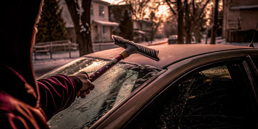 Person using a large ice scraper on a frosty car windshield at dawn