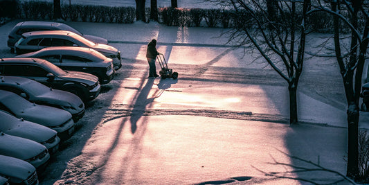 A person using a long-handled snow broom to quickly clear snow off multiple cars.