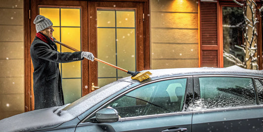 Man using a snow brush to quickly remove snow from the roof of a car.