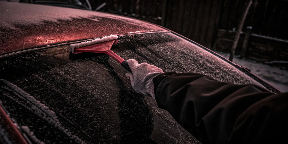 Gloved hand wiping down a red ice scraper after clearing snow from a windshield