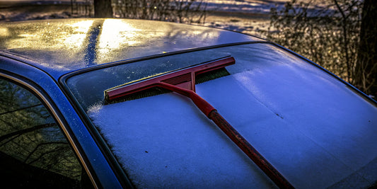 The Edge oversized red snow and ice scraper resting on a snow-covered car windshield