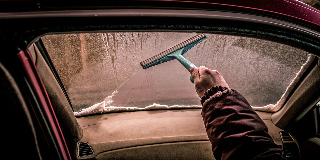 Using an ergonomic ice scraper to clear frost from a car windshield.