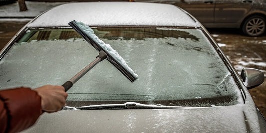 Snow brush and wide snow scraper beside a snow-covered car