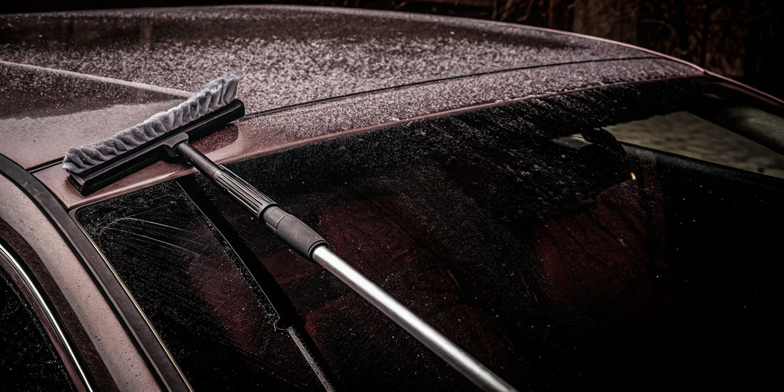 A snow scraper clears the top layer of snow from a windshield, preparing to tackle the ice.