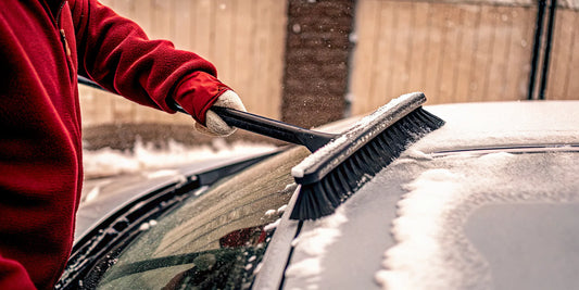 A telescoping snow scraper clearing thick snow from a car windshield.