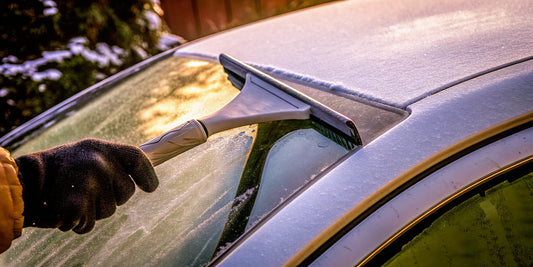 A car window scraper clearing thick ice and frost from a car's windshield.