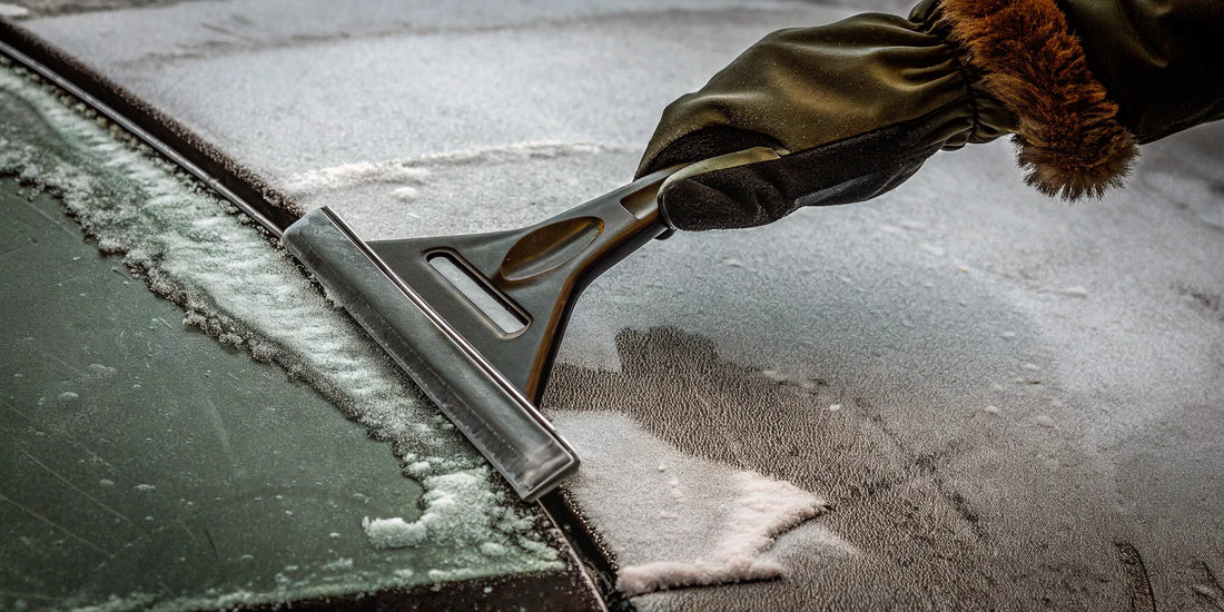 A hand in an ice scraper glove clearing a frosty car windshield.