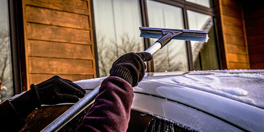 A person using one of the widest snow scrapers to clear ice from a car windshield.