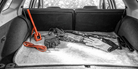 Winter car survival kit essentials laid out on car trunk showing ice scraper, blanket, flashlight, and emergency gear in snowy conditions