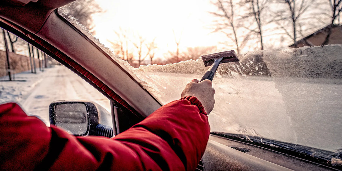 Driver using a quality ice scraper on a frosty windshield in snowy conditions