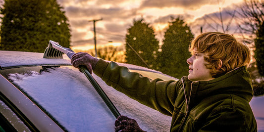 New teen driver clearing snow and ice off a car windshield in a snowy driveway