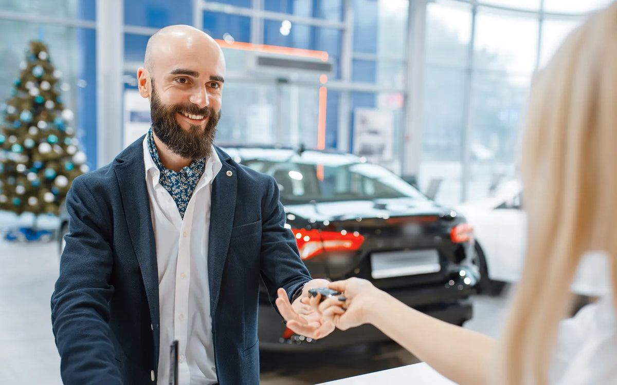 A salesperson hands car keys across the desk in a showroom with a Christmas tree
