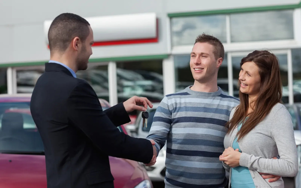 A salesperson hands keys to a smiling couple outside a dealership