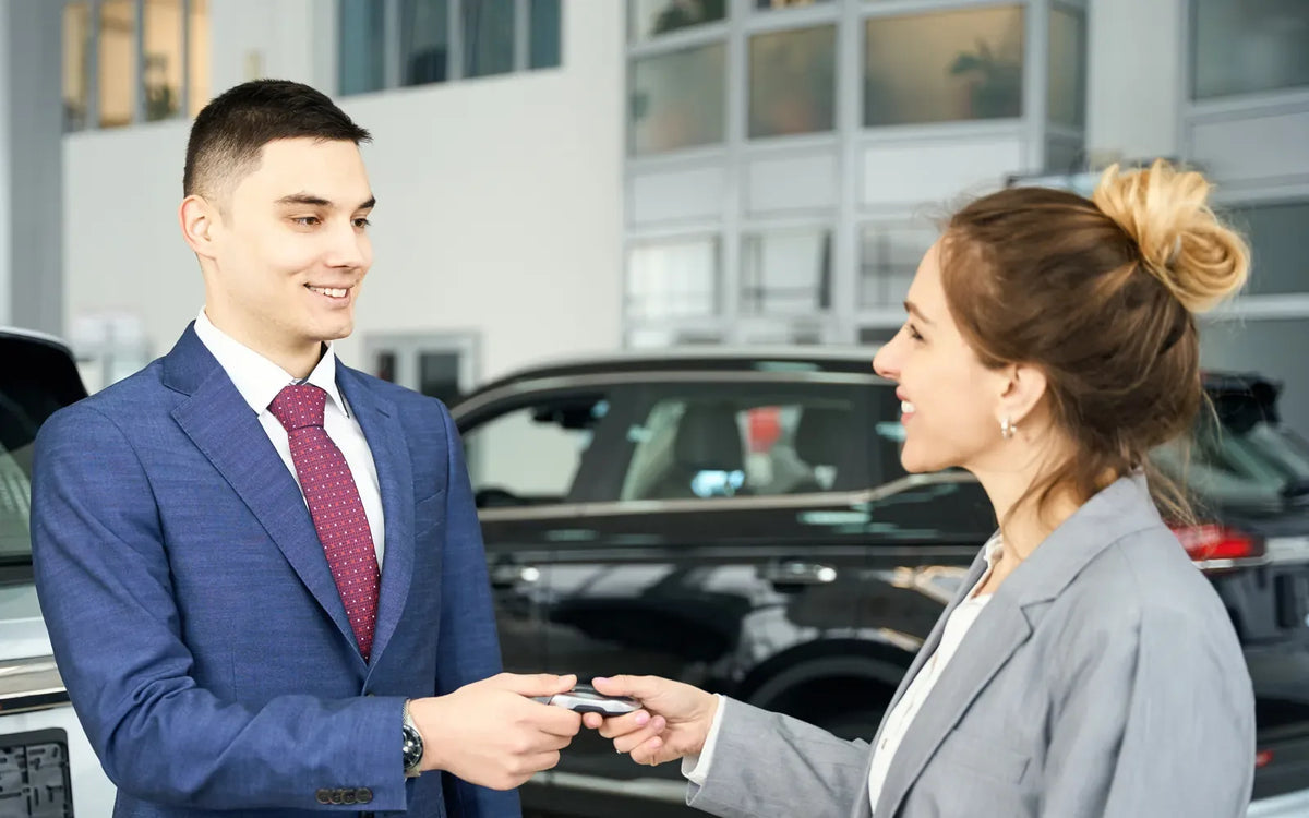 A salesperson hands a key fob to a customer in a showroom