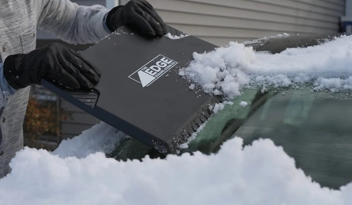 Two gloved hands pushing The EDGE across a snowy windshield, snow sliding off its edge